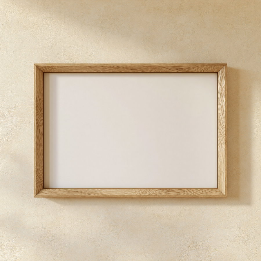 A wide flat profile natural white oak wood picture frame mounted on a soft cream plaster wall. The frame has a blank pure white interior and no glass, with visible light grain and a realistic drop shadow.