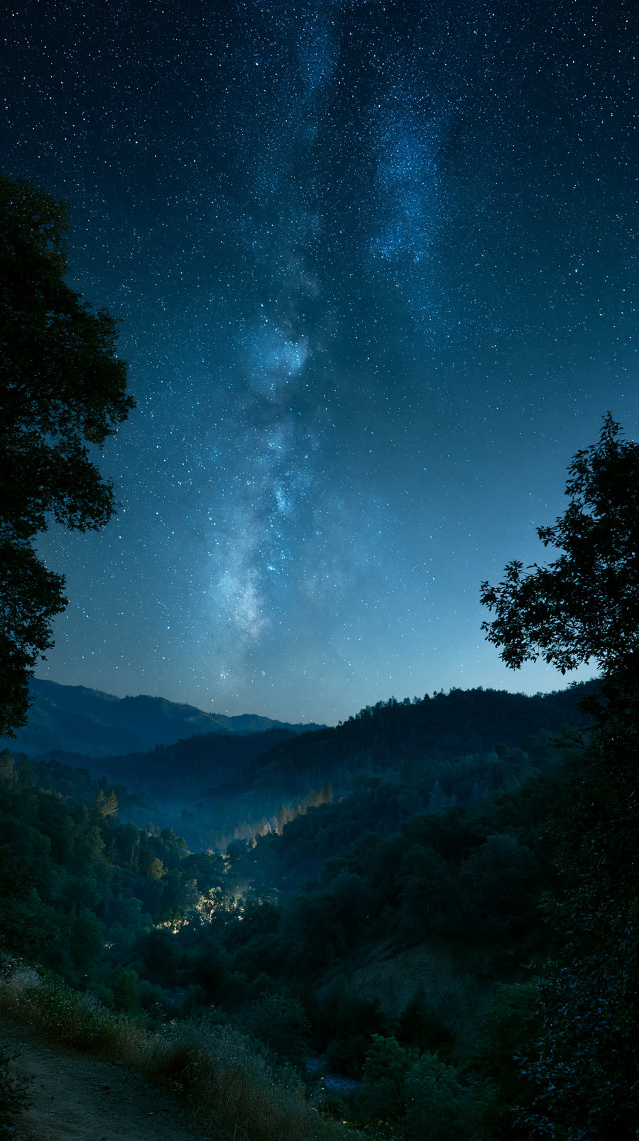 A vast night sky filled with stars and the visible Milky Way over a mountainous landscape, with deep blue tones and a melancholic atmosphere.